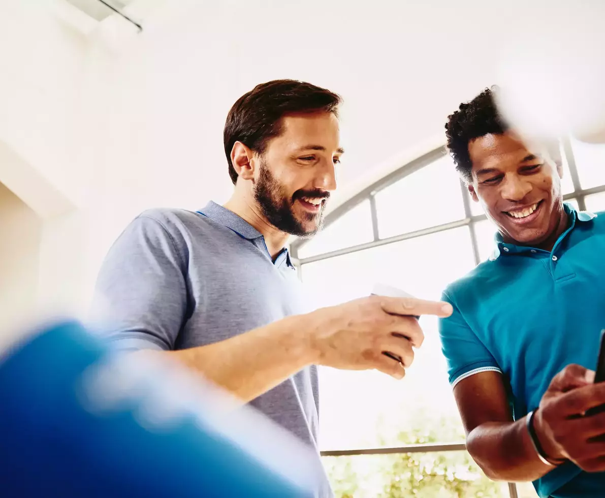Two smiling colleagues (men) looking at a phone.
