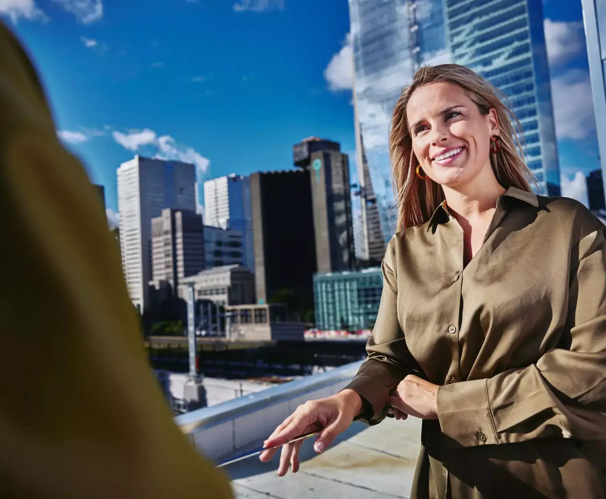 Female smiling, standing outside on a balcony talking to a person