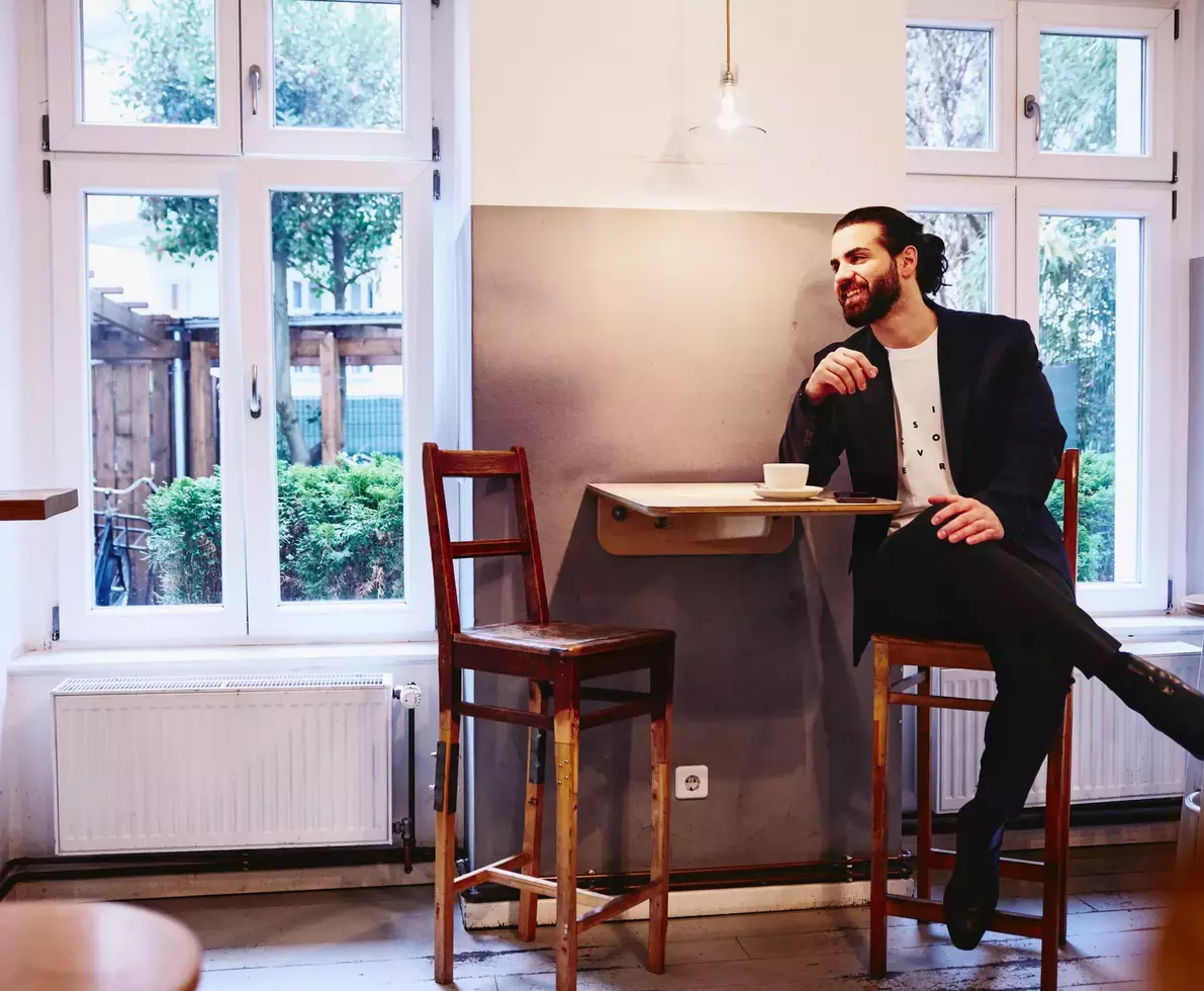 male sitting at table with a coffee, smiling looking away.
