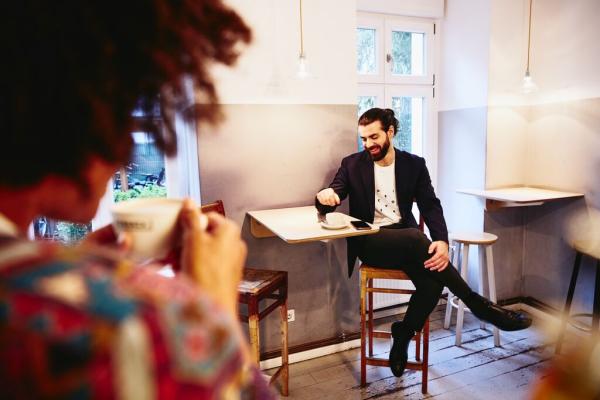 Man sitting at a table with coffee, looking down while having a conversation with someone.