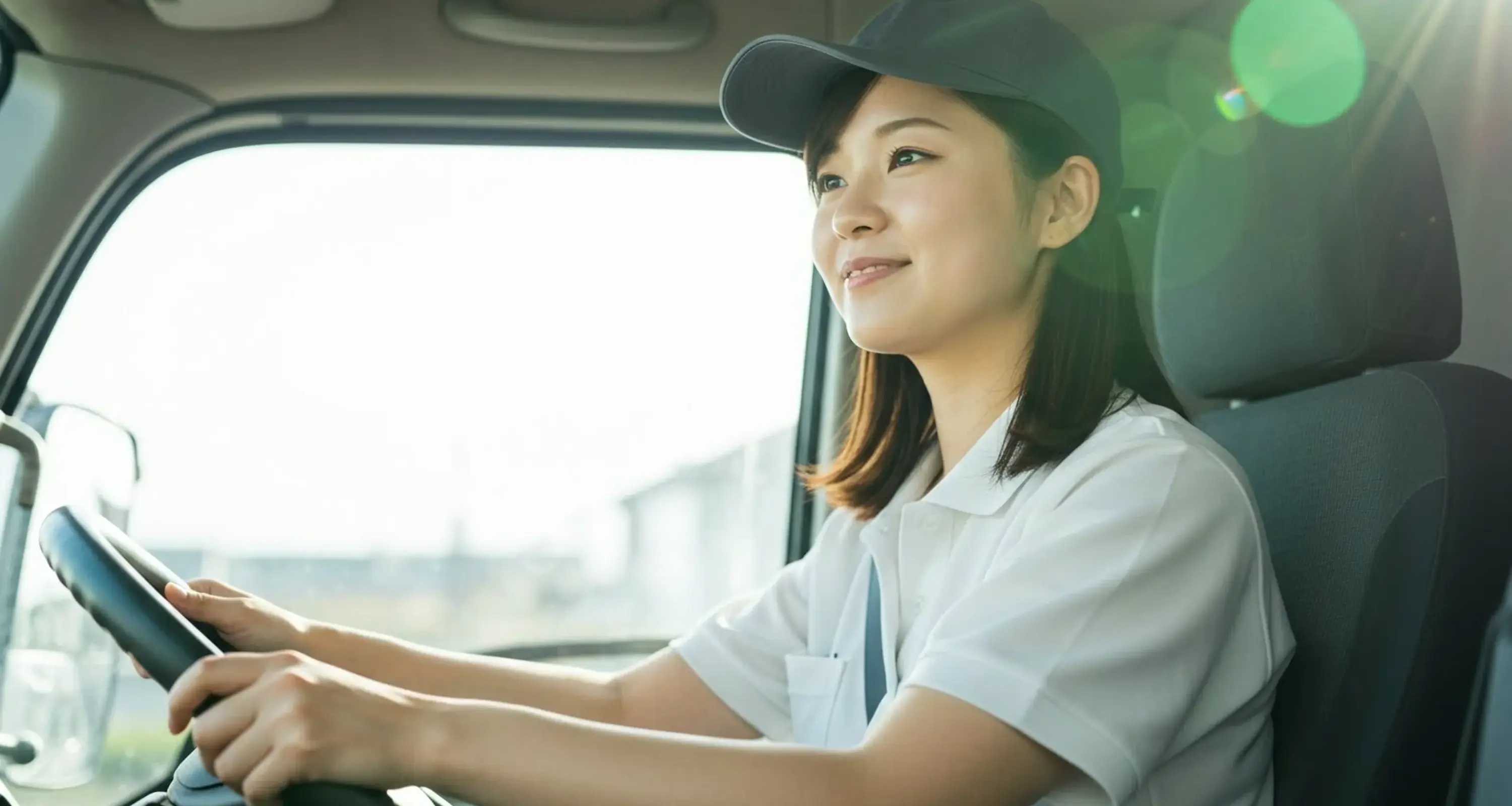 an asian woman driving a truck, focused on the road ahead, with a cityscape visible through the windshield