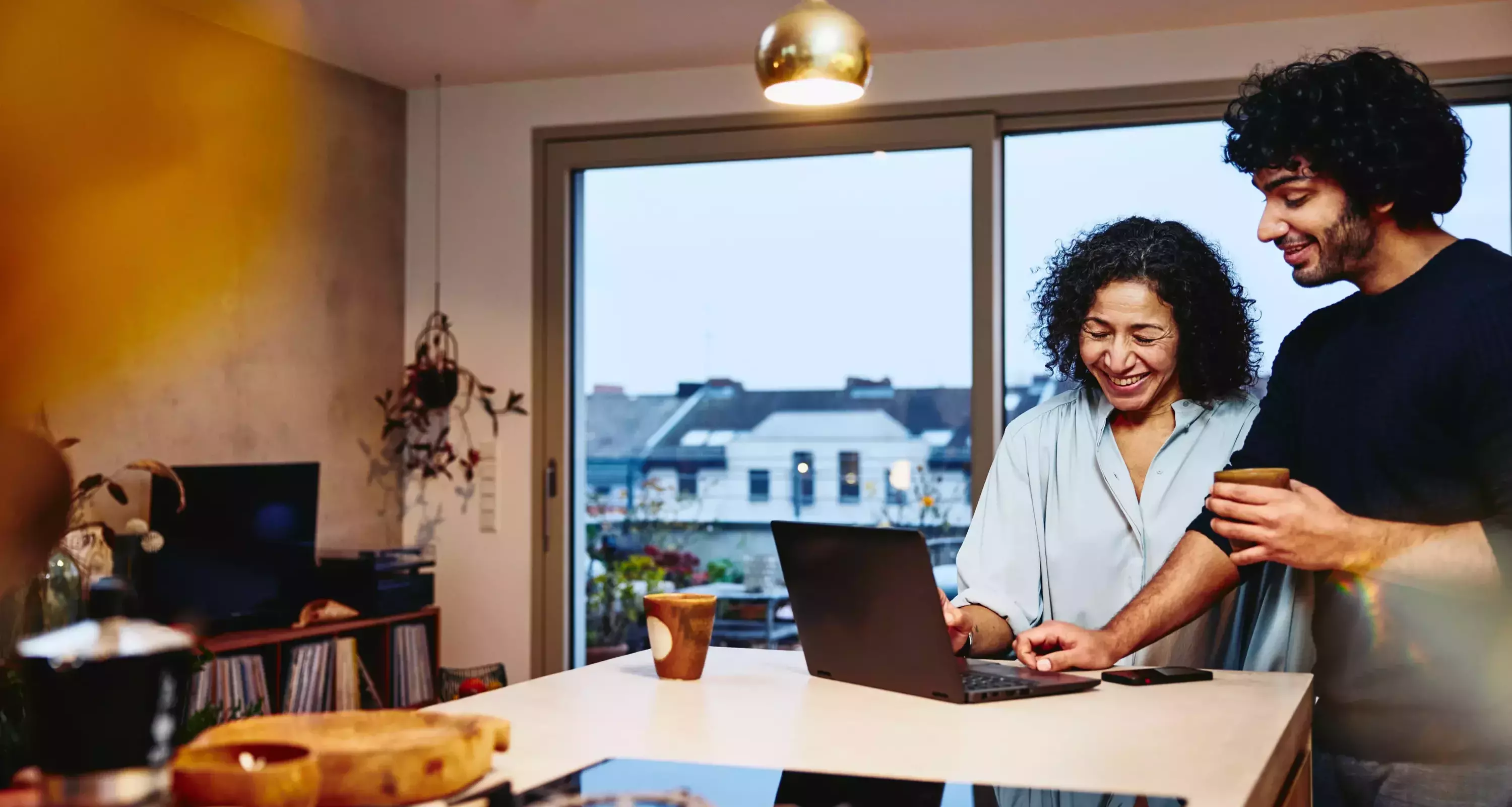 Womale and male standing next to the kitchen counter top, looking at a laptop. Smiling.
