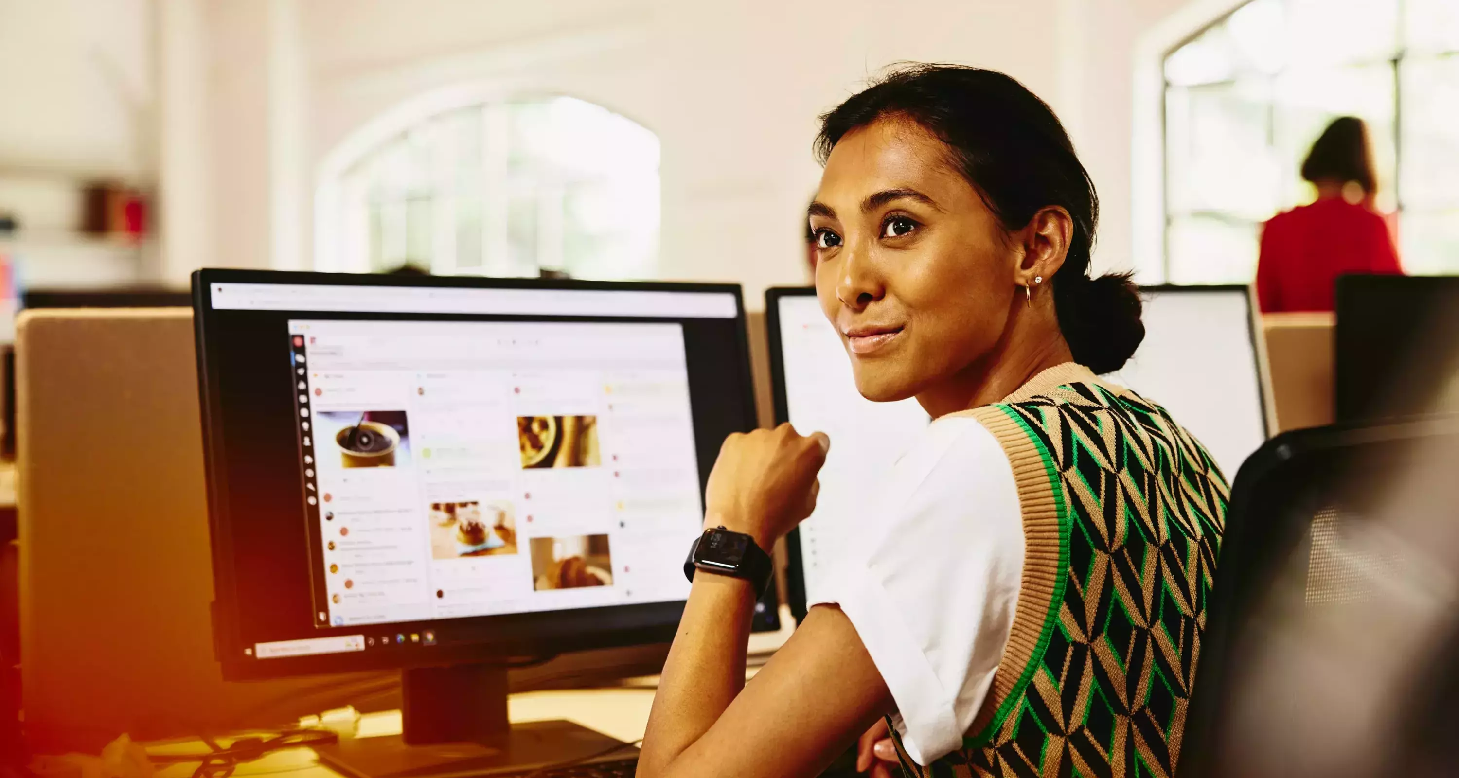 Womale sitting at her desk, looking away from computer screens displaying marketing content.
