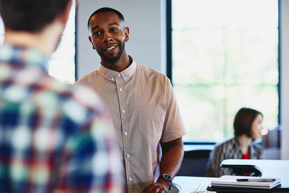 a man talking to his colleague with a woman in the background working