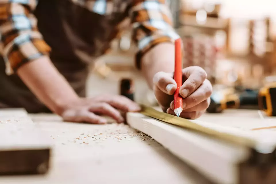 Cropped view of man holding pencil near wooden plank and measuring tape.