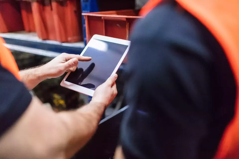 Close up of two workers using tablet computer at factory warehouse. Foremen with colleague using digital tablet in warehouse.