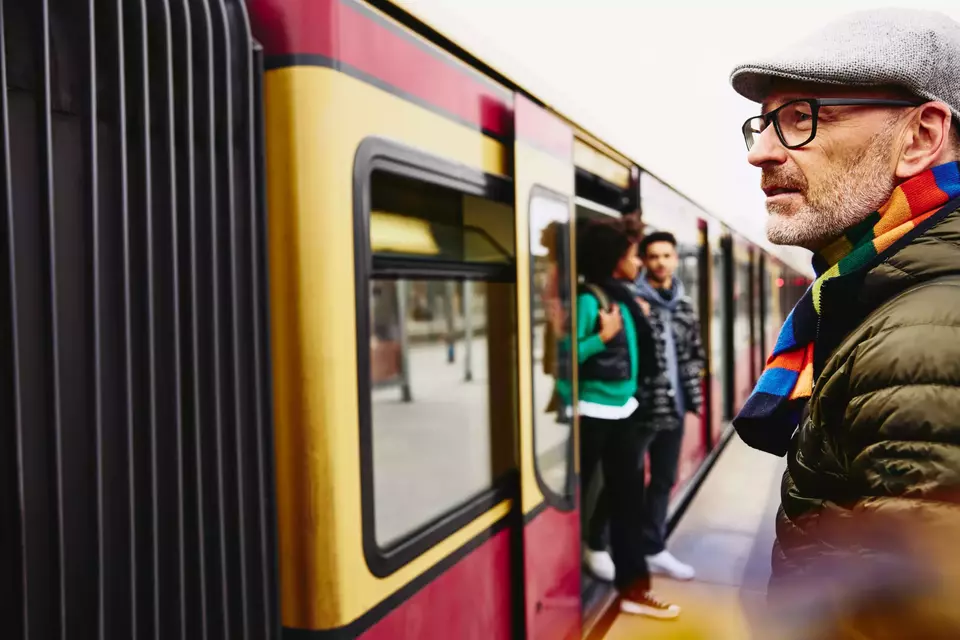 male standing next to a train. Two people getting out of a train in the background.

