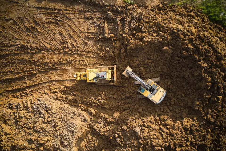 Bulldozer is scraping a layer of soil and excavator is digging and dumping dirt