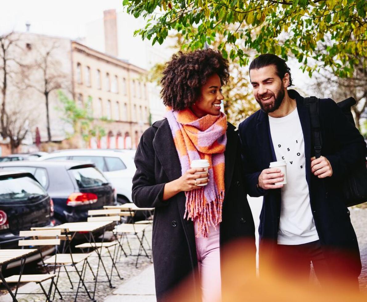 Smiling man and woman having a conversation while holding drinks and walking outside. Smiling man and woman having a conversation while holding drinks and walking outside.